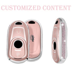 Może przedstawiać: Różowo-złote osłony na kluczyki do samochodu ze srebrnym wykończeniem. Jedna osłona ma rząd małych różowych kryształków. Tekst "CUSTOMIZED CONTENT" znajduje się na górze. Osłony mają okrągły przycisk i symbole klucza.