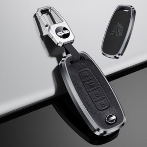May include: A black and silver car key fob with a leather texture. The fob has a silver border and a silver key ring attachment. The key fob has buttons for lock, unlock, and trunk release. The Nissan logo is visible on the key fob.