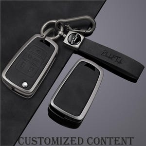 May include: A set of black car key fobs with silver trim, a matching key fob cover, and a black leather key strap. The strap is engraved with the name "Elizabeth Taylor". The words "CUSTOMIZED CONTENT" are at the bottom.