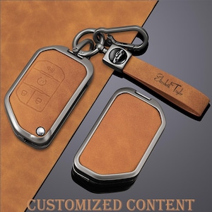 May include: A set of brown leather key fob covers with a silver-colored metal frame. One cover is attached to a key ring and a leather strap with the name "Elizabeth Taylor" engraved. The image also includes the text "CUSTOMIZED CONTENT".