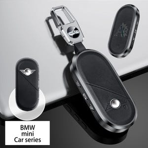 May include: A black car key fob with a silver metal frame and a silver key ring. The fob has a leather-like texture and a silver emblem. The text "BMW mini Car series" is in a white rectangle.