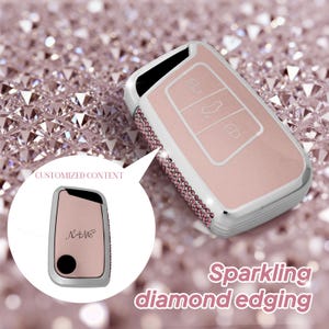 May include: A pink car key fob cover with a silver frame and sparkling diamond edging. The cover has three buttons and the text "Sparkling diamond edging". A smaller image shows a similar cover with the word "NAME".