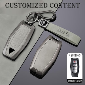 May include: A set of car key fobs and a key chain. The key fobs are gunmetal gray with embossed button icons. The key chain has a gray leather strap with the name "Elizabeth Taylor" and a silver clasp. The image also includes the text "4 BUTTONS" and "APPLICABLE CAR KEYS."