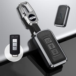 Może przedstawiać: Czarny skórzany brelok do kluczy samochodowych ze srebrnymi wykończeniami i pasującym brelokiem. Brelok posiada przyciski do blokowania, odblokowywania i innych funkcji. Pokazany jest również osobny klucz z literą "A".