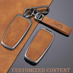 Pode incluir: Um conjunto de chaveiros de couro castanho com molduras e ferragens de metal prateado. Um chaveiro tem um design em relevo, e outro tem uma correia de couro com o nome "Elizabeth Taylor" impresso. As palavras "CUSTOMIZED CONTENT" estão na parte inferior.