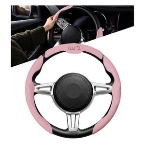 May include: A pink and black steering wheel cover with the text "Elizabeth Taylor". The cover has a textured pink grip area and a black leather-like trim. The steering wheel has silver accents.