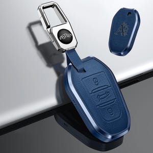 May include: A blue leather car key fob with a silver metal keychain. The fob has embossed key symbols and a silver frame. An additional blue key fob cover with the letter "A" is also shown.
