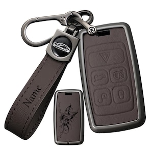 May include: A dark brown leather key fob cover set with a gunmetal carabiner and a matching strap featuring the engraved word Name. The set includes a larger rectangular key fob case with five embossed button icons and a smaller rectangular piece.