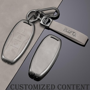 May include: A set of car key fobs with a matching keychain. The key fobs are light grey with a metallic silver trim. The keychain strap is light grey and has the name "Elizabeth Taylor" printed on it.