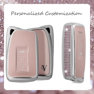 May include: A set of light pink car key fob covers with silver metallic edges. One cover features a side panel encrusted with small pink crystals and the letter V with a floral accent. The text Personalized Customization appears above the items.