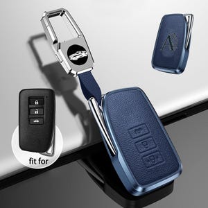 以下が含まれることがあります： 青い革製の車のキーフォブカバー、シルバーの金属フレームとマッチするキーチェーン。 キーフォブにはエンボス加工されたボタンとキーチェーンに車のロゴが付いています。 「fit for」の文字が見えます。