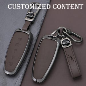 May include: Two car key fobs with brown leather and silver-tone metal casing. One fob has a leather strap with a silver-tone metal clasp. The text "CUSTOMIZED CONTENT" is at the top of the image.
