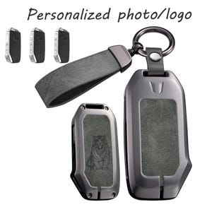 Könnte beinhalten: Ein dunkelgraues Autoschlüssel-Etui aus Metall mit einer strukturierten grauen Einlage, einer Tigergravur auf einer Seite und einem passenden grauen Lederband mit Metallring. Der Text Personalized photo/logo ist oben zu sehen.