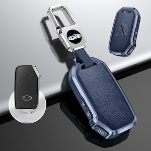 May include: A selection of car key fobs in different designs. The main fob is navy blue with a silver frame and a matching leather strap connected to a silver keyring. The keyring has a car silhouette. Other fobs are black and navy blue.