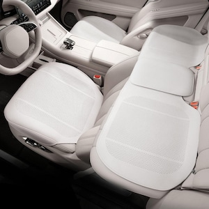 Puede incluir: Fundas blancas para asientos de coche con diseño perforado. Las fundas están instaladas en un coche con interior blanco, incluyendo el volante, el salpicadero y la consola central. Los asientos tienen una estética moderna y minimalista.