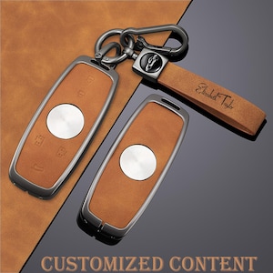 Puede incluir: Dos llaveros de coche de cuero marrón claro con detalles plateados y un llavero a juego. Los llaveros tienen un botón plateado y ribete plateado. El llavero tiene una correa de cuero con el nombre "Elizabeth Taylor" y un logotipo de coche.