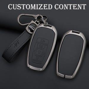 May include: A black leather key fob with a gunmetal-colored metal frame and a matching key ring. The key fob has embossed buttons and a leather strap with the initials "MF". The text "CUSTOMIZED CONTENT" is at the top.