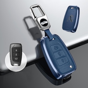 May include: Blue car key fob cover with a silver metal key ring. The fob has three buttons and a car logo. A separate key fob cover with the letter "A" is also shown. The key fob is blue with a textured leather-like appearance.