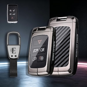 May include: A set of two metallic car key fobs with carbon fiber patterns and the text Speed Concepts, alongside a separate key fob and a metal keychain featuring the letter E and a floral design, all displayed against a dark background.