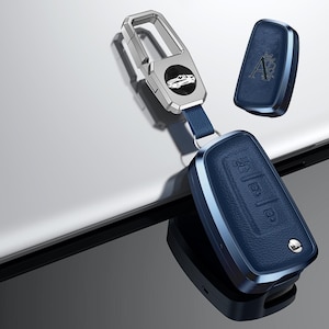 May include: A set of car key accessories, including a key fob cover and a key chain. The key fob cover is navy blue with a silver trim and embossed buttons. The keychain has a silver car emblem.