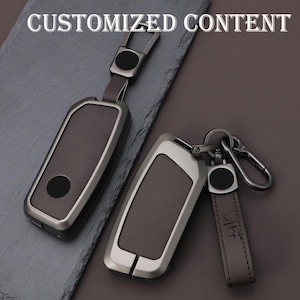 May include: Two car key fobs with leather and metal casing. The key fobs are brown and silver, with a black circle on the front. One fob has a leather strap with the initials "JHF". The text "CUSTOMIZED CONTENT" is at the top.