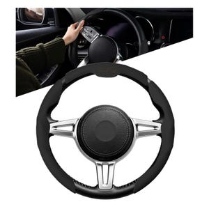 May include: Black and silver car steering wheel with a leather grip. The wheel has a central hub with a stitched leather cover and silver spokes. The image shows a hand on the wheel, suggesting use in a vehicle.