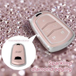 Puede incluir: Un llavero de coche en oro rosa con un borde plateado con diamantes. La llave tiene botones para bloquear, desbloquear y otras funciones. La imagen también muestra un llavero con el texto "CUSTOMIZED CONTENT" y "NAME".