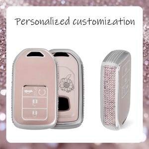 Könnte beinhalten: Eine hellrosa Autoschlüsselhülle mit silbernem Metallrand und einem Sonnenblumen-Strichzeichnungsmotiv. Die Seite der Hülle ist mit kleinen rosa Kristallen besetzt. Der Text Personalized customization steht über den Schlüsselhüllen.