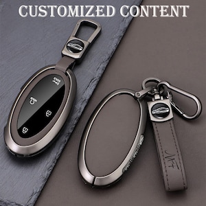 May include: Two car key fobs with keychains. The key fobs are oval-shaped with a dark gray metallic finish and a black screen. One keychain has a leather strap with the initials "MFF". The text "CUSTOMIZED CONTENT" is at the top.