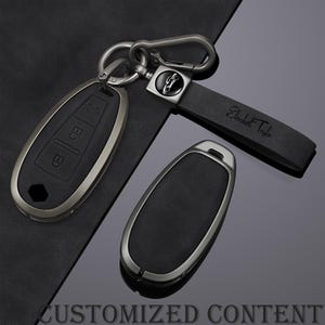 Peut inclure: Ensemble de clés de voiture noires avec garniture argentée. L'une est attachée à un porte-clés et à une lanière en cuir noir avec le nom "Elizabeth Taylor" en relief. Le texte "CUSTOMIZED CONTENT" est également visible.