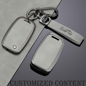May include: A set of car key accessories in a light gray color. The set includes a key fob cover, a keychain with a leather strap, and a metal clasp. The strap is engraved with the name "Elizabeth Taylor". The words "CUSTOMIZED CONTENT" are at the bottom.