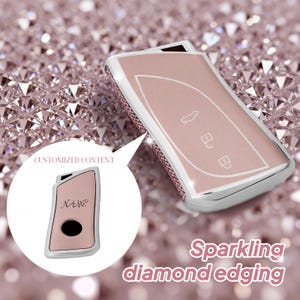Puede incluir: Una funda para llave de coche en oro rosa con un marco plateado y bordes de diamantes brillantes. La funda tiene iconos de llave y el texto "CUSTOMIZED CONTENT" y "NAME".
