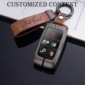 May include: A gunmetal gray car key fob with a leather strap. The strap is brown and has the name "Mark Frederick" printed on it. The key fob has white icons for car functions. The words "CUSTOMIZED CONTENT" are at the top.