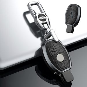 May include: A black leather car key fob with silver accents and a matching key. The fob has three buttons and a silver circle in the center. The key ring has a silver car emblem.