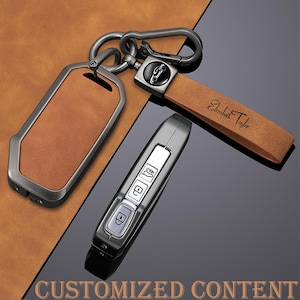 May include: A set of car keys and accessories. The set includes a brown leather key fob, a metal key ring, and a car key. The key fob has a metal frame and the name "Elizabeth Taylor" is engraved on the leather strap. The image also includes the text "CUSTOMIZED CONTENT".
