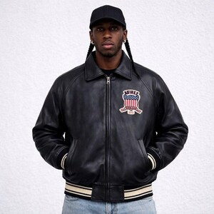 Puede incluir: Chaqueta de cuero negra con cuello, cierre de cremallera y parche en el pecho. El parche presenta un dise&ntilde;o rojo, blanco y azul con el texto "AVIREX ESTABLISHED 1975". La chaqueta tiene pu&ntilde;os y cintura a rayas.