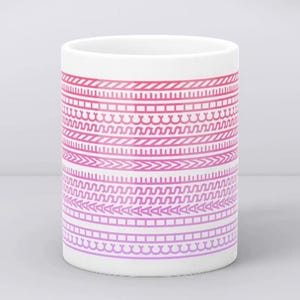 Könnte beinhalten: Eine weiße Keramiktasse mit einem umlaufenden Design aus rosa und lila geometrischen Mustern. Die Muster umfassen Linien, Zickzacklinien und andere Formen. Die Tasse ist zylindrisch und hat eine glatte Oberfläche.