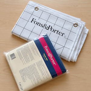 May include: A white Fons & Porter design wall featuring a black grid pattern and metal grommets, accompanied by its original packaging. The packaging is a clear plastic sleeve with a blue and pink label displaying the Fons & Porter brand name.