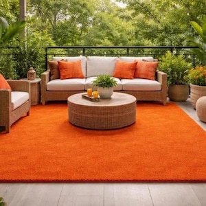 May include: An outdoor patio scene featuring an orange rug, wicker furniture, and potted plants. The setting includes a sofa, two armchairs, and a round coffee table, creating a comfortable space. The rug measures approximately 3 x 3.6 metres.