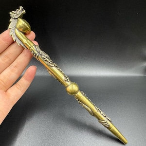May include: A long, cylindrical brass-colored metal pipe featuring an intricate dragon motif. The top end is shaped like a dragon head with a bowl, while the shaft is decorated with embossed dragon scales and a central spherical accent piece.