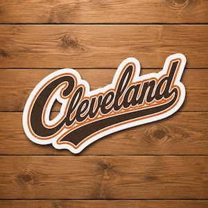 Puede incluir: Una pegatina con el logotipo de Cleveland en blanco, marrón y naranja sobre un fondo de madera. La palabra "Cleveland" está escrita en una fuente cursiva estilizada con un contorno y una sombra marrones.