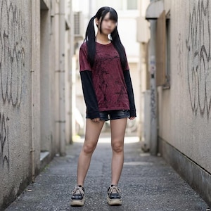 Peut inclure: Une personne porte un t-shirt à manches longues bordeaux et noir avec un motif texturé, un short en jean et des baskets à plateforme. La tenue est portée dans une ruelle avec des graffitis sur les murs.