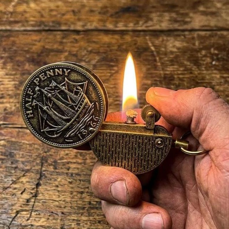 Vintage-style brass coin lighter inspired by old British half penny designs. The lid features an engraved ship and the inscription “Half Penny 1966,” giving it a classic maritime look. Made from durable metal with an aged brass finish, it uses a traditional wick and flint ignition system. The detailed coin design and textured body create a unique retro collectible with a strong old-world aesthetic.