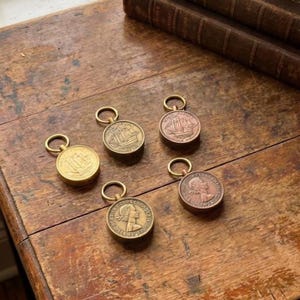 May include: Five antique brass keychains with coin-shaped pendants. The pendants feature ship and portrait designs. The keychains are arranged on a rustic wooden surface, with a stack of old books in the background.