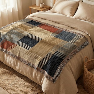 May include: A woven throw blanket featuring a geometric pattern of rectangular blocks in shades of navy blue, rust orange, and tan. The blanket has a textured surface with visible vertical and horizontal thread lines and a fringed edge on all sides.