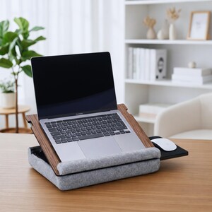 Op de afbeelding: Een laptop staat op een laptoptafel van hout en grijs vilt. De tafel heeft een ingebouwd muismatje en een grijs vilten kussen voor comfort. De laptop is opengeklapt en toont een leeg scherm.