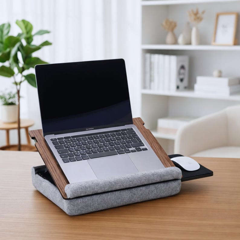 Op de afbeelding: Een laptop staat op een laptoptafel van hout en grijs vilt. De tafel heeft een ingebouwd muismatje en een grijs vilten kussen voor comfort. De laptop is opengeklapt en toont een leeg scherm.
