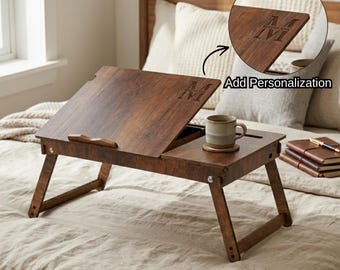 May include: A wooden bed tray with folding legs, featuring a dark brown finish. The tray has an adjustable top and a small compartment for a mug and coaster. The text "Add Personalization" is visible. The tray is engraved with the letters "M" and "I".