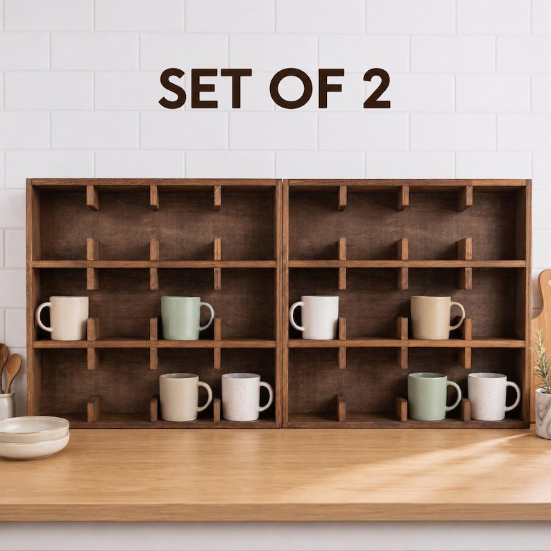 May include: A set of two dark brown wooden wall-mounted display shelves with multiple square compartments. The text SET OF 2 is displayed above the shelves. Several solid-colored ceramic mugs in white, cream, and light green are placed inside.