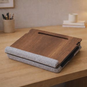 Op de afbeelding: Een houten laptoptafel met een donkerbruine afwerking en een grijze vilten polssteun. De tafel heeft een sleuf voor een tablet of telefoon en is ontworpen om op schoot of op een bureau te worden gebruikt. De tafel is opgevouwen.